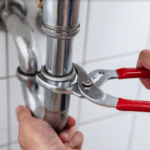 Hand gripping under-sink pipe while grasping it with a wrench in the other hand.