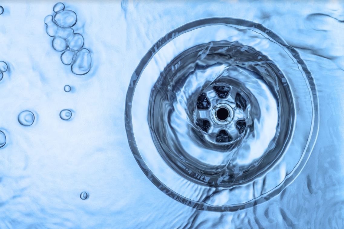 Clear water going down a drain in a stainless steel sink.