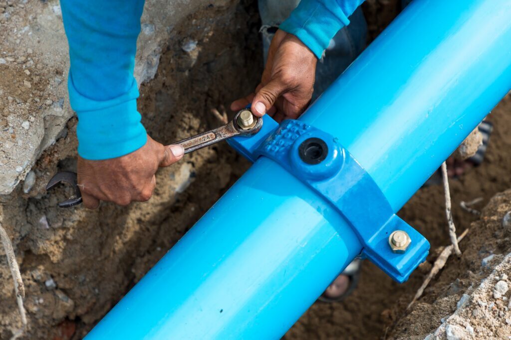 Man using a large wrench on water pipes. Construction site with new Water Pipes in the ground